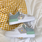 Stylish white sneakers with green accents and daisy embroidery on a yellow gingham fabric background, perfect for casual fashion enthusiasts.