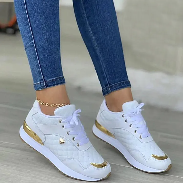 White women's sneakers with gold accents, quilted design, and heart detail, paired with blue jeans. Fashionable casual footwear for women.