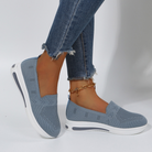 Blue slip-on sneakers with white soles, worn with frayed hem jeans. Stylish women's casual footwear, breathable mesh design, perfect for everyday comfort.