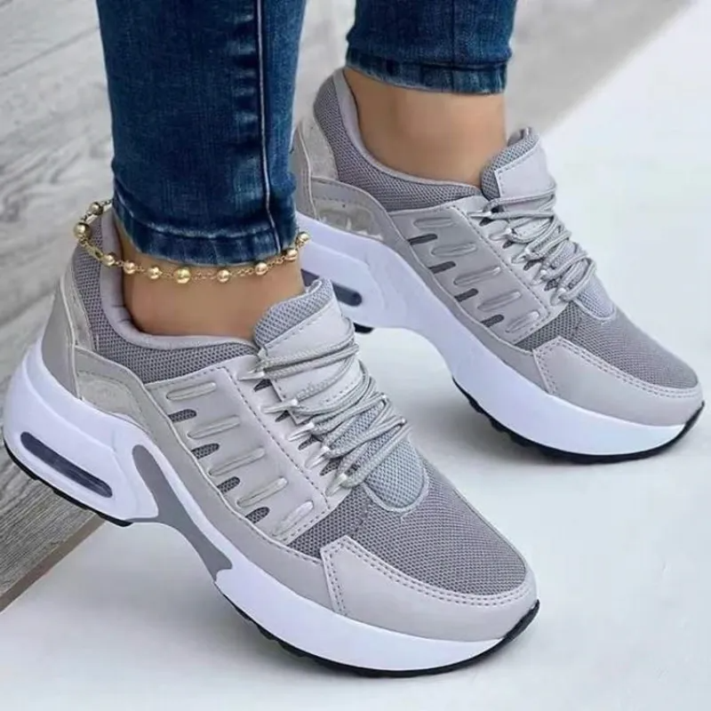 Gray women's athletic sneakers with white soles, mesh upper, and lace-up design, worn with jeans. Stylish, comfortable footwear for casual wear.