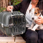 Person holding a small dog next to a green pet carrier with a transparent door, ideal for pet travel and transport.