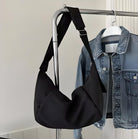 Black shoulder bag with adjustable strap hanging on a metal rack beside a denim jacket; stylish accessory for casual outfits, modern fashion.