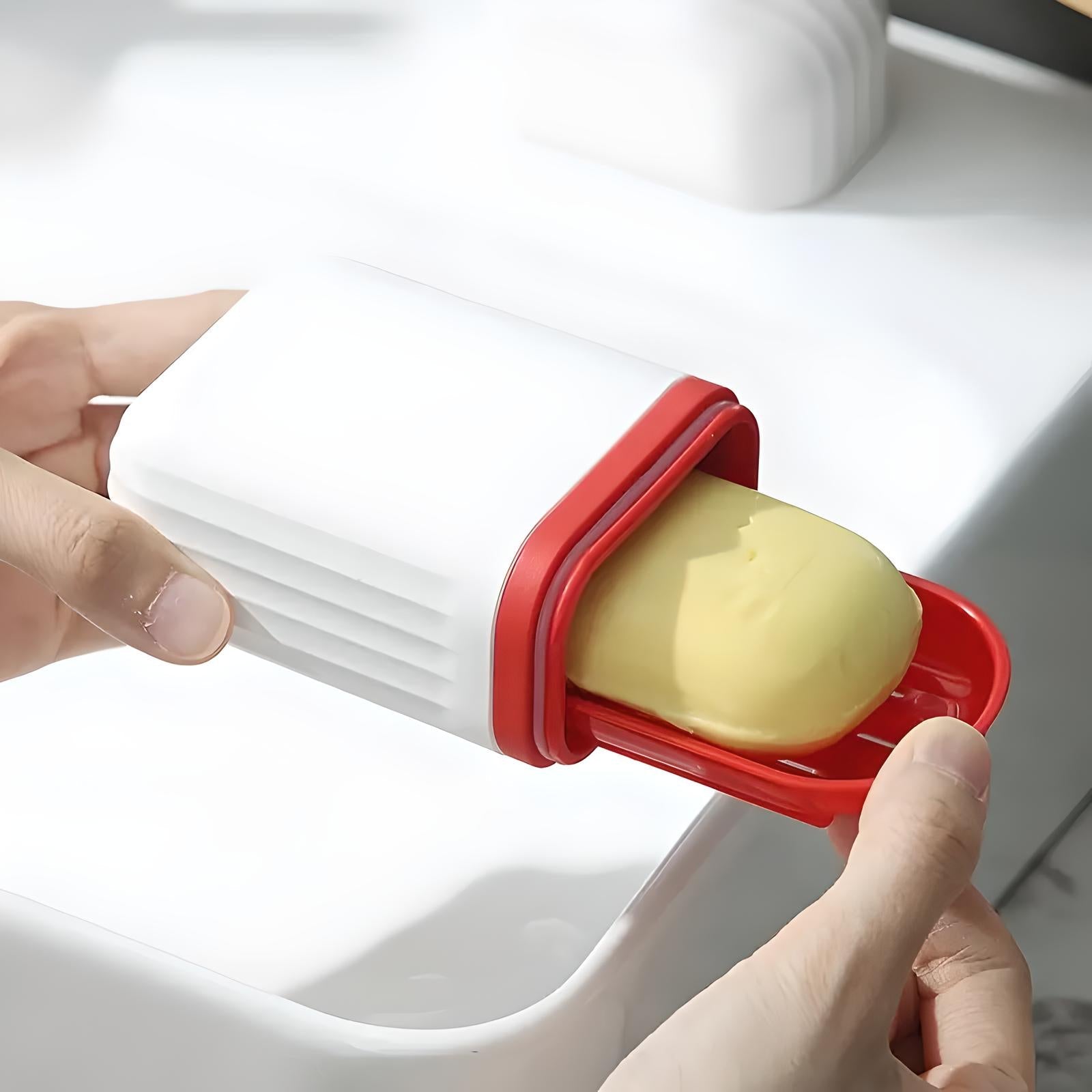 Hands holding a white butter dispenser with a red slider, dispensing a stick of butter. Kitchen gadget, butter storage, easy spreader.