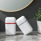 Minimalist white wireless earbuds cases with red and gray accents on marble surface, modern design, next to a green plant and round mirror.