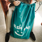 Person holding a large teal laundry bag with "wash me" text and smiley face, sitting on a chair. Ideal for laundry storage and organization.