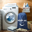 Modern front-loading washing machine in a cozy laundry room with wooden walls, surrounded by folded towels, detergent bottles, and a "wash me" laundry bag.