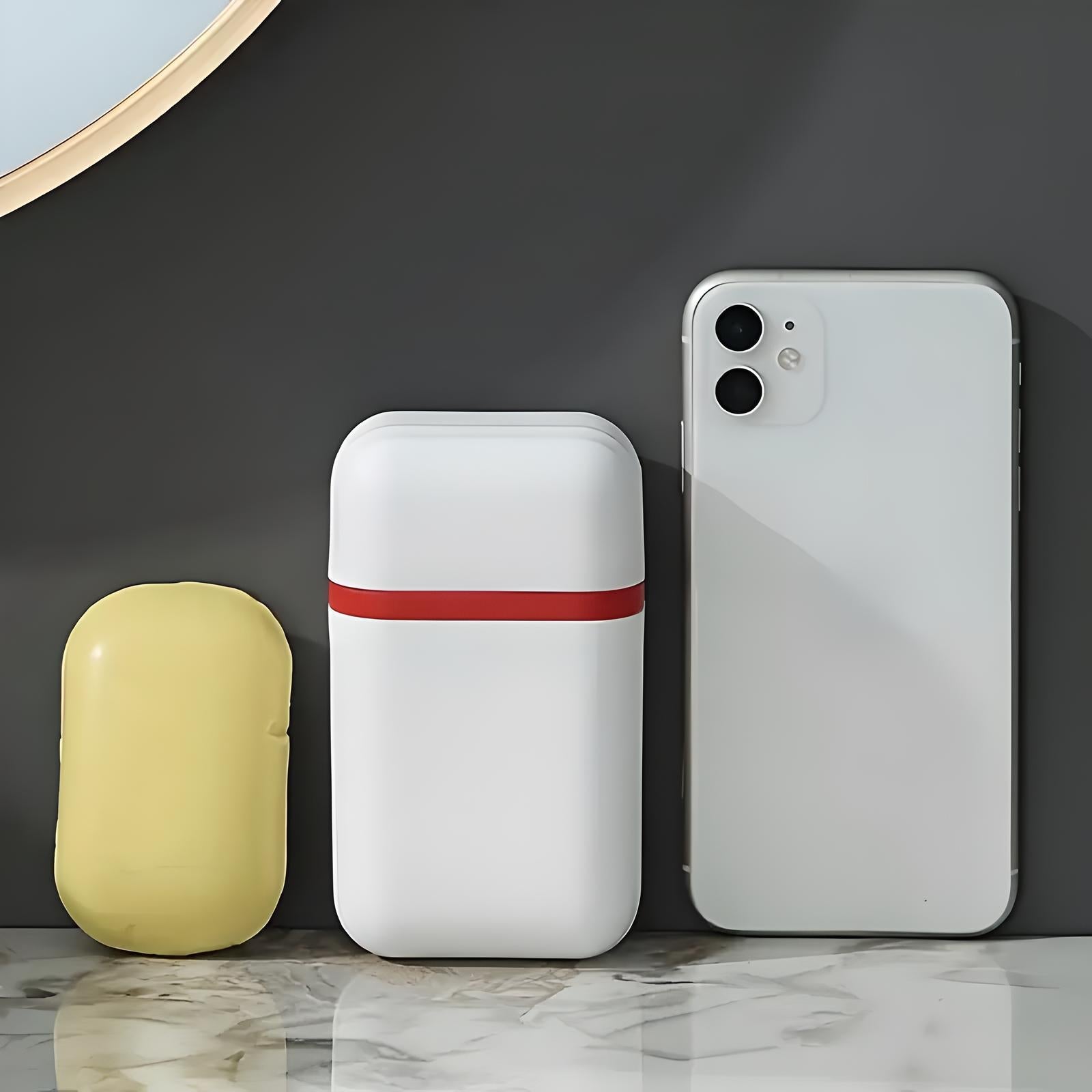 White wireless earbud case with red stripe, yellow soap bar, and smartphone on marble surface. Modern tech accessories and hygiene essentials.