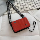 Red crossbody bag with "Forever Young" strap on a checkered background. Stylish, compact design ideal for travel and daily use. Fashion accessory.