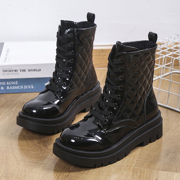 Black patent leather combat boots with quilted design, thick soles, and lace-up front on wooden floor. Fashionable women's footwear for fall.