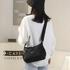 Woman wearing a black bucket hat and white shirt, carrying a stylish black crossbody bag with a woven pattern, standing in a modern cafe setting.