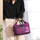 Woman holding a stylish purple travel handbag with black accents, featuring silver zippers and a sleek design, perfect for fashion-forward travelers.