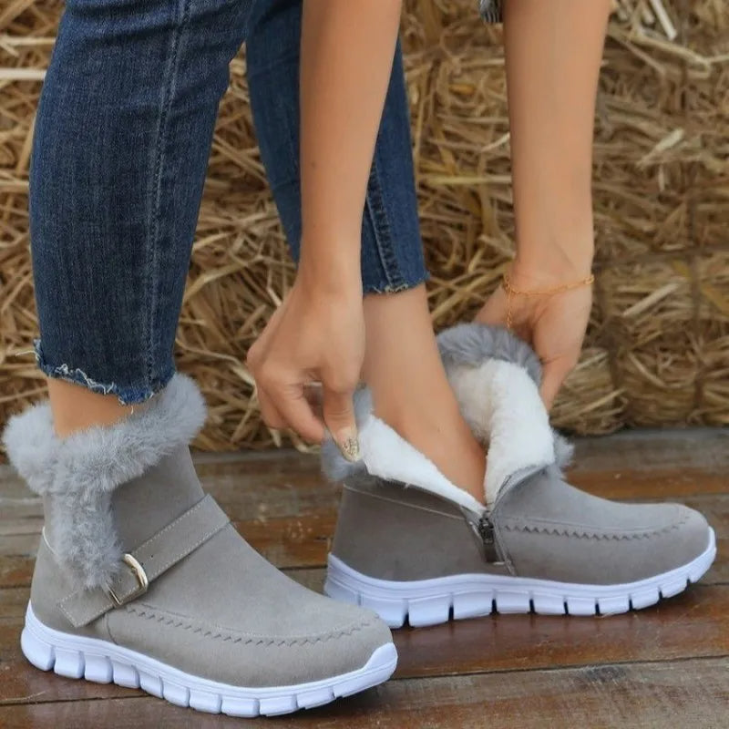 Woman wearing gray fur-lined ankle boots with white soles, adjusting zipper. Stylish winter footwear, casual jeans, wooden background. Cozy fashion.