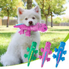 Fluffy white dog holding a pink dinosaur plush toy in a park, with green and blue dinosaur toys displayed below. Perfect pet chew toys for playful dogs.