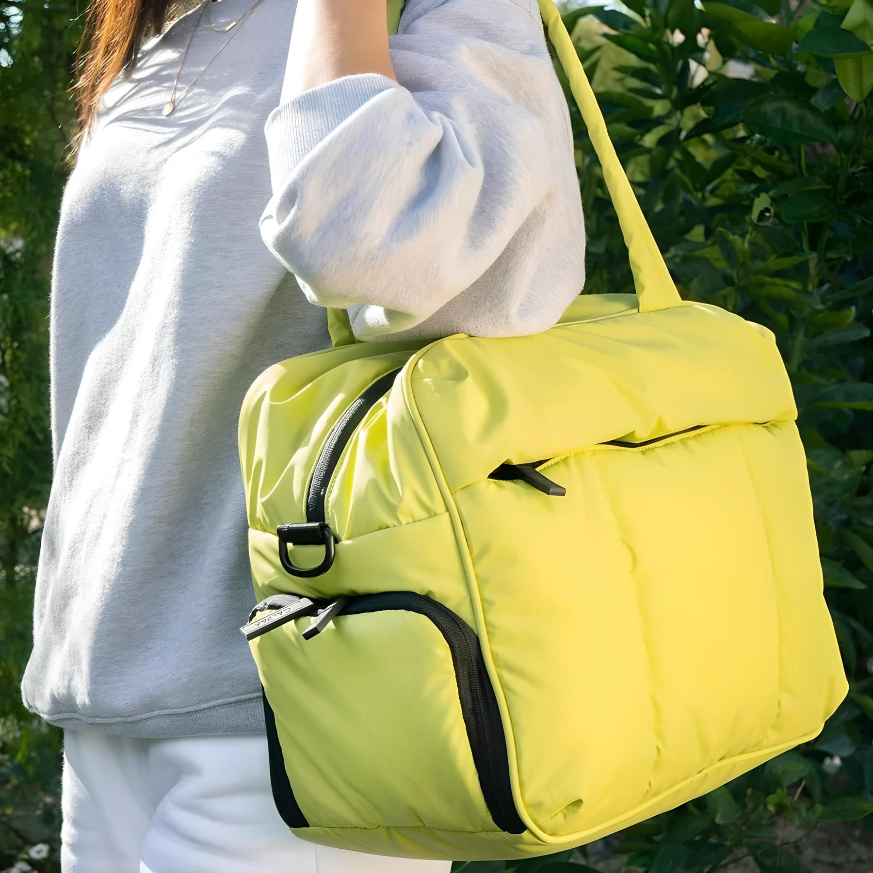 Woman carrying a stylish yellow puffer tote bag with black accents, wearing a gray sweatshirt. Perfect for fashion, travel, and casual outings.