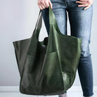 Woman holding large green leather tote bag, wearing blue jeans. Fashionable, spacious handbag for shopping or travel. Stylish accessory for women.