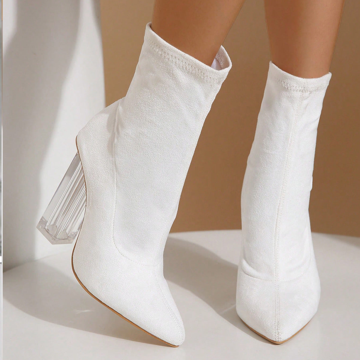 White ankle boots with clear block heels, featuring a sleek pointed toe design. Perfect for fashion-forward outfits and trendy footwear collections.