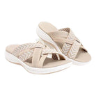 Beige women's slip-on sandals with crisscross straps, cushioned footbed, and white sole. Comfortable summer footwear, casual style.