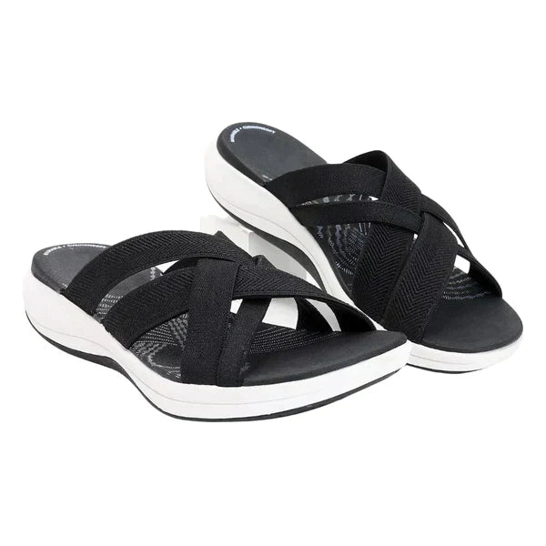 Black crisscross strap slip-on sandals with cushioned footbed and white sole, perfect for casual wear. Comfortable women's summer footwear.