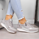 Women's stylish gray sneakers with metallic accents, paired with light blue ripped jeans, showcasing trendy casual footwear fashion.