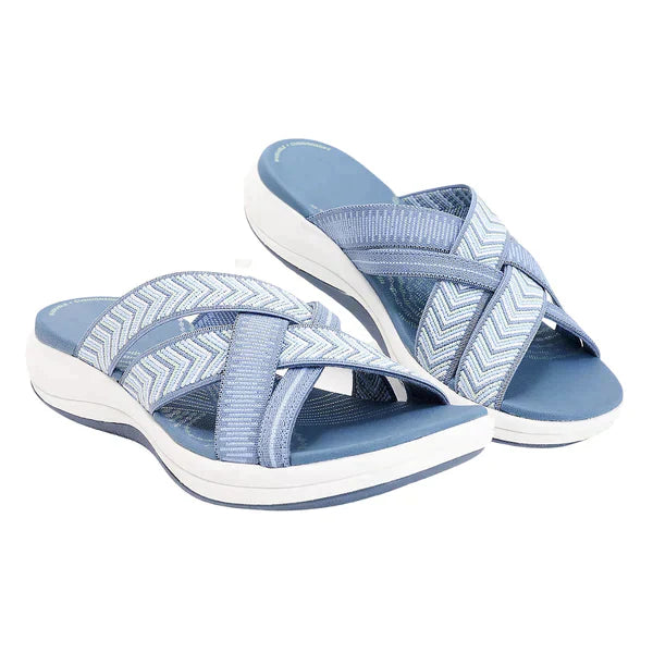 Light blue women's slip-on sandals with crisscross straps, chevron pattern, and cushioned white sole. Perfect for casual summer wear and comfort.