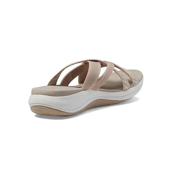 Beige women's slip-on sandal with crisscross straps, cushioned footbed, and white sole. Comfortable summer footwear for casual wear.