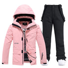 Pink women's ski jacket with hood and black ski pants set, waterproof winter sportswear.