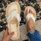 Beige woven flip-flops with textured straps, held by a hand, on a pebble background. Perfect for summer fashion, beachwear, and casual outings.