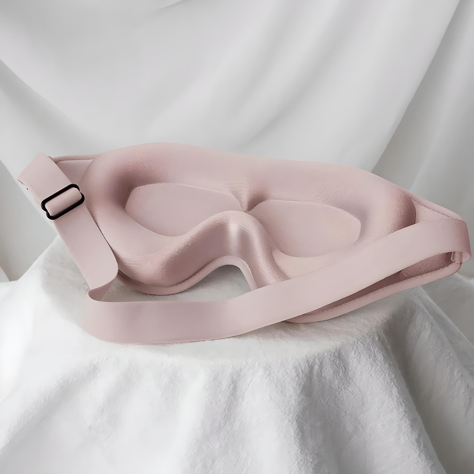 Soft pink sleep mask with adjustable strap on white fabric background, designed for comfort and light blocking. Ideal for travel and relaxation.