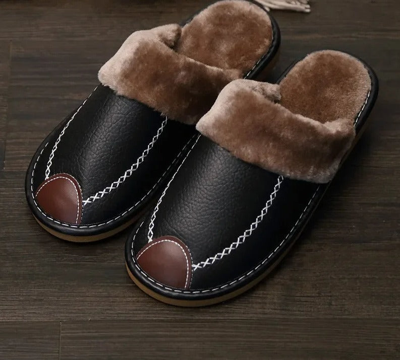 Black leather slippers with brown faux fur lining, white stitching, and brown toe accents on a dark wooden floor. Cozy winter footwear.