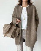 Woman wearing a cozy brown cardigan over a white shirt, holding a stylish beige leather handbag. Fashionable casual outfit with accessories.