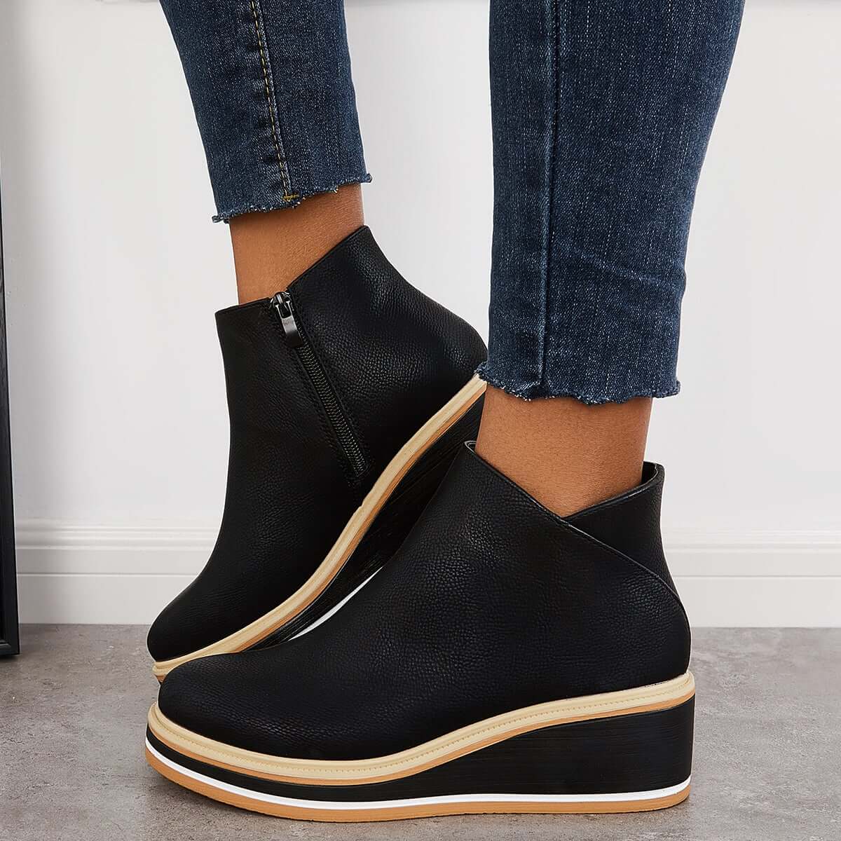 Black leather wedge ankle boots with side zipper, paired with frayed hem skinny jeans. Stylish women's footwear for casual and trendy outfits.