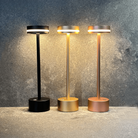 Modern LED table lamps in black, gold, and rose gold with sleek design, illuminating against a textured gray background. Stylish home lighting decor.