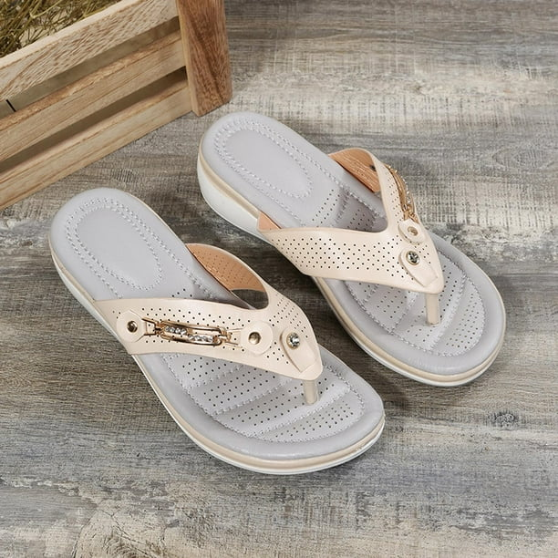 Beige women's orthopedic sandals with perforated design, cushioned sole, and decorative metal accents on wooden floor background.