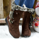 Brown faux fur-lined winter boots with buckle straps, worn with blue jeans, standing on snow. Cozy, stylish footwear for cold weather.