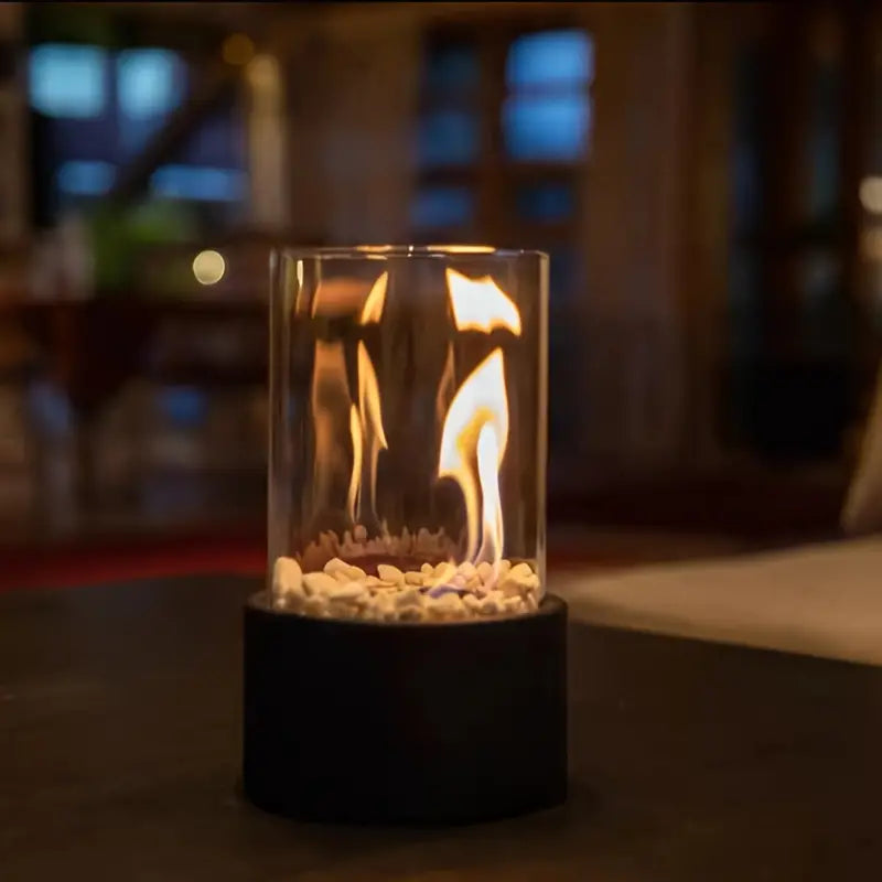 Modern tabletop fire pit with glass cylinder, black base, and decorative stones, creating a cozy ambiance. Ideal for indoor and outdoor use.