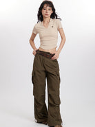 Woman wearing beige V-neck crop top and olive green cargo pants, standing against a white background. Fashionable casual outfit, trendy style.