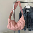 Pink shoulder bag hanging on a metal rack beside a denim jacket. Fashionable accessory, soft fabric, adjustable strap. Stylish women's handbag display.