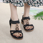 Women's black sandals with rhinestone embellishments, open-toe design, and ankle strap, paired with a floral dress. Fashionable summer footwear.