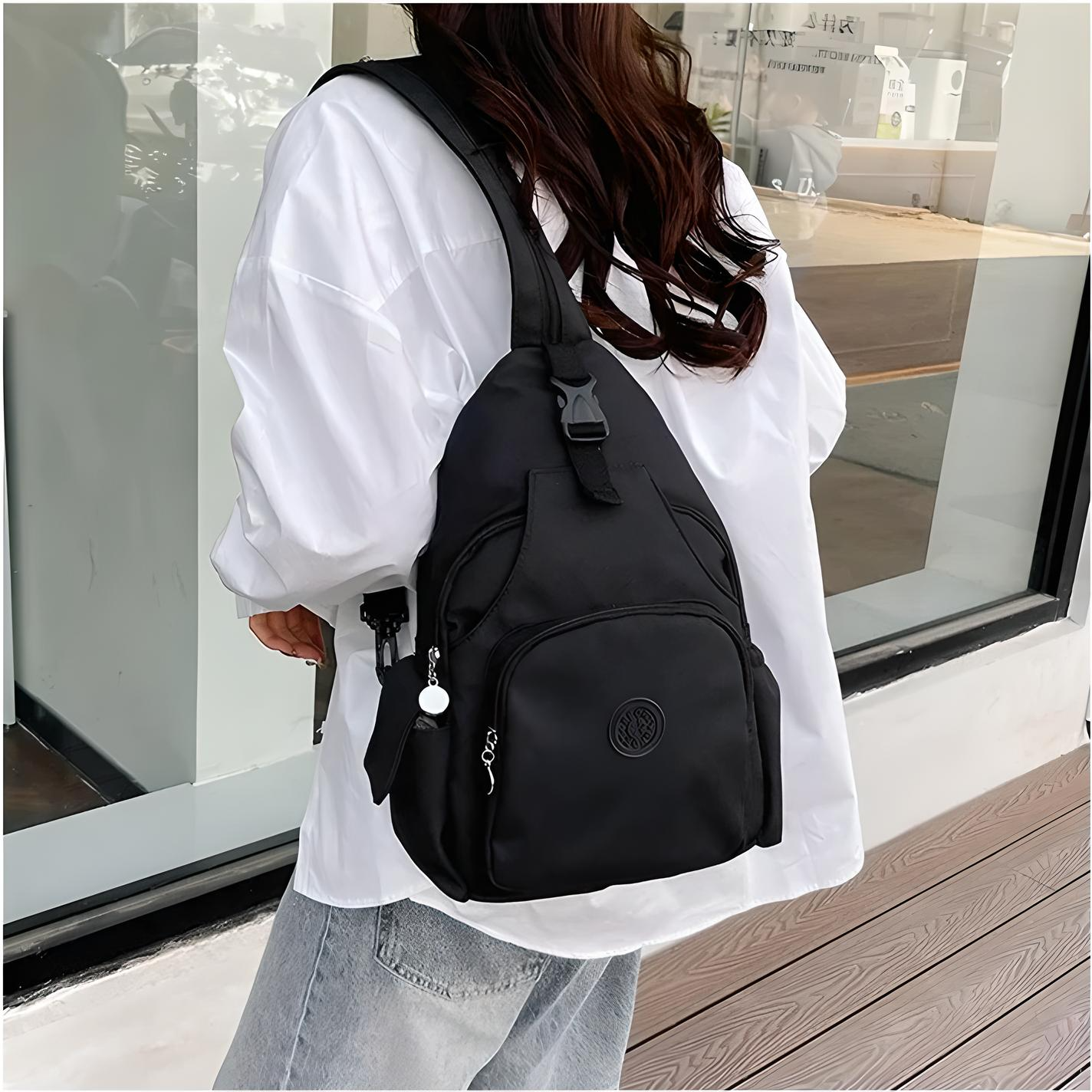 Woman wearing a stylish black crossbody backpack with multiple compartments, paired with a white shirt and jeans, standing outdoors. Fashion accessory.