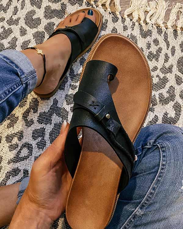 Black leather sandals with buckle detail, held by a person wearing jeans, on a patterned rug. Stylish summer footwear, casual fashion accessory.