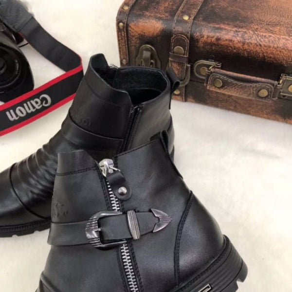 Black leather boots with zipper and buckle detail, Canon camera strap, and vintage suitcase on a white background. Fashion accessories display.