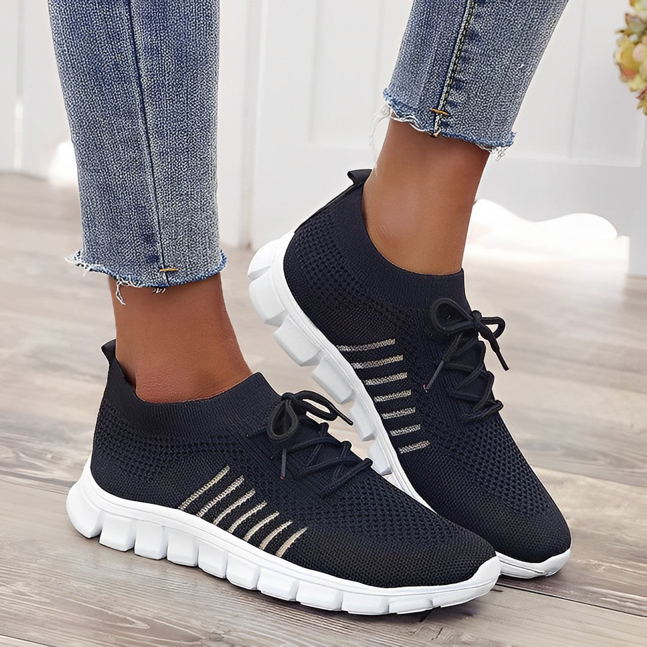 Black knit sneakers with white soles and striped detailing, worn with blue jeans. Stylish, comfortable footwear for casual wear.