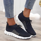 Black knit sneakers with white soles and striped detailing, worn with blue jeans. Stylish, comfortable footwear for casual wear.