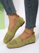 Yellow knit loafers on feet with denim jeans, featuring a gold anklet. Stylish women's footwear, casual fashion, comfortable slip-on shoes.