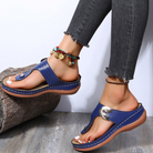 Blue orthopedic sandals with thick soles, worn with frayed hem jeans and colorful anklets, on a wooden floor. Fashionable, comfortable footwear.