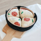 Plush pizza toy set with four slices featuring pepperoni and green toppings, displayed in a black fabric pan on a wooden board; perfect for kids.