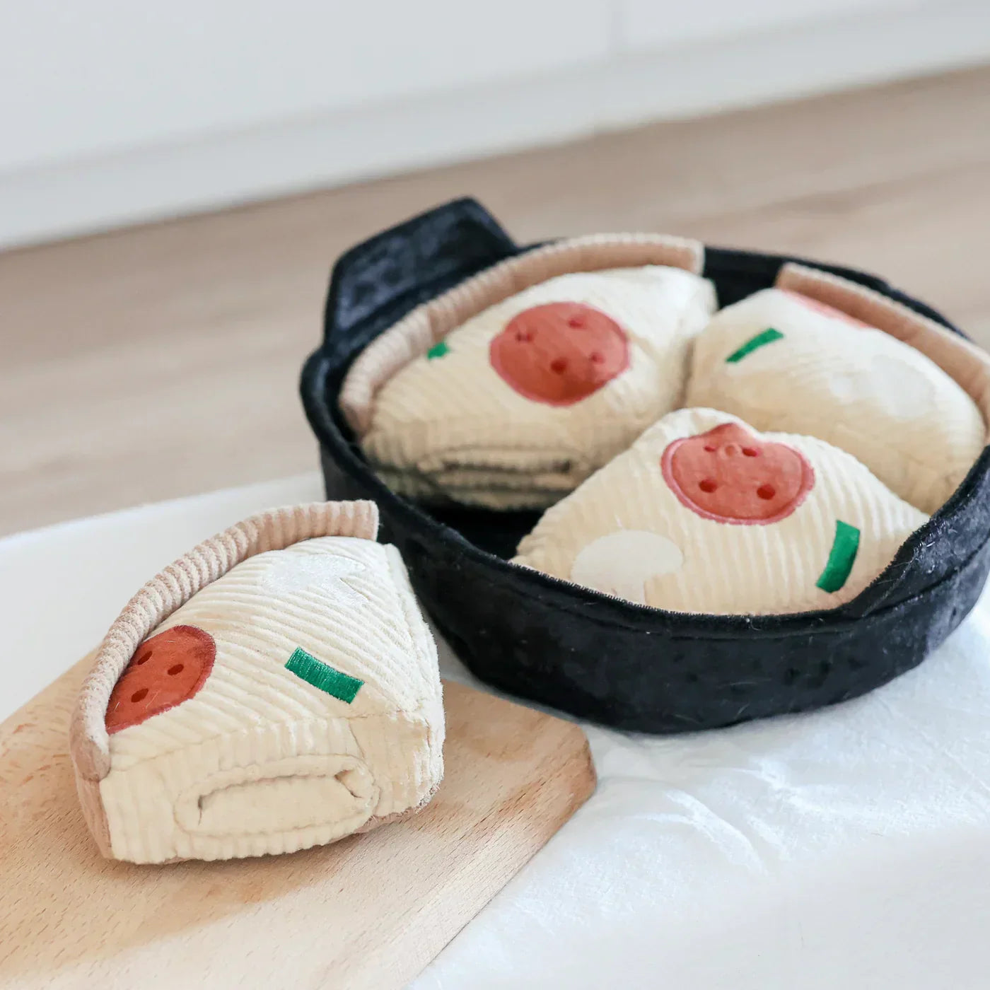 Plush toy dumplings in a black fabric pan on a wooden board, featuring embroidered details. Perfect for kids' play, kitchen-themed decor, or gifts.