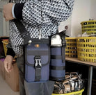 Man carrying a stylish blue crossbody bag with a water bottle holder, standing in a room with yellow baskets. Fashionable accessory, practical design.