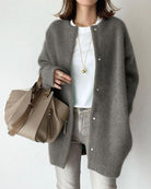 Woman wearing a gray wool cardigan over a white shirt, holding a beige leather handbag. Fashionable casual outfit, stylish fall clothing.