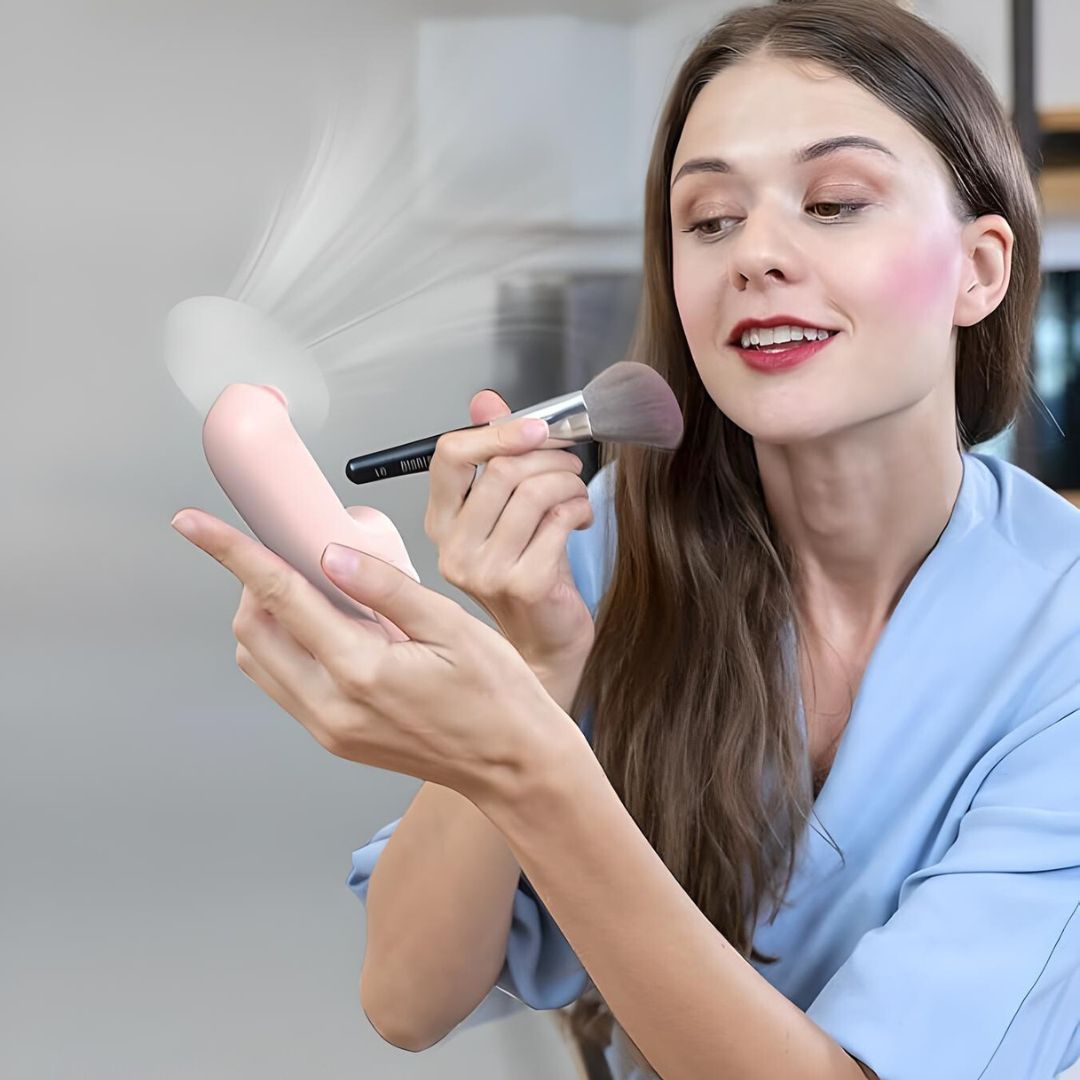 Woman applying makeup with a brush, holding a pink facial cleansing device. Beauty routine, skincare, makeup application, home setting.